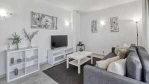 Un salon moderne avec un canapé gris, une table basse blanche et un téléviseur à écran plat posé sur un meuble de télévision blanc.