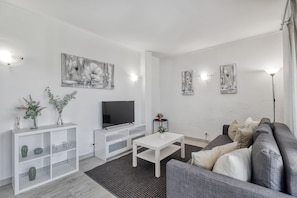 A modern living room with a grey sofa, white coffee table, and a flat-screen TV on a white entertainment unit. - T NIS Golf SEA in Vilamoura (Loulé)