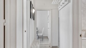 Un couloir aux murs blancs, avec un banc, une chaise et une porte donnant sur une autre pièce.