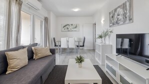 Un salon moderne comprenant un canapé, une table basse, un téléviseur, un coin repas et des œuvres d’art.