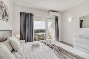 Ein Hotelzimmer mit Bett, Schminktisch, einem Balkon mit Vorhängen und einer Klimaanlage.