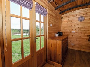 A wooden cabin interior with a large window, a wooden cabinet, and a clock on the wall. - The Damselfly (Driffield)