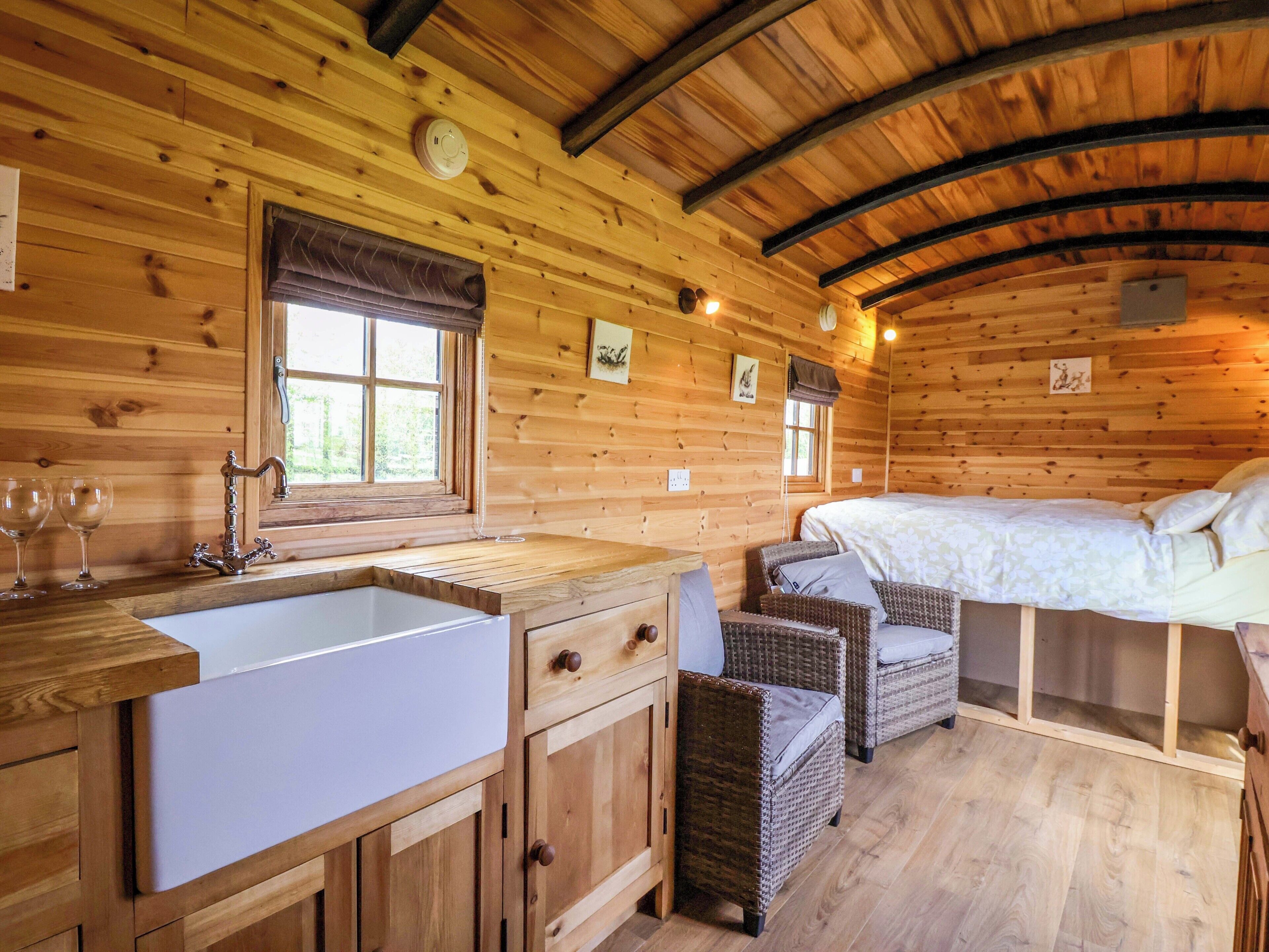 L’intérieur d’un chalet en bois, avec un lit, des chaises en osier, un évier et une fenêtre.