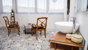 A bathroom with a large window, two wooden chairs, a round table, a white sink, and a mirror.