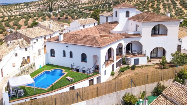 A white villa with a swimming pool, arched windows, and a view of olive groves.