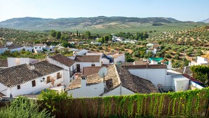 A rural village with white buildings, terracotta roofs, and a hilly landscape in the background.
