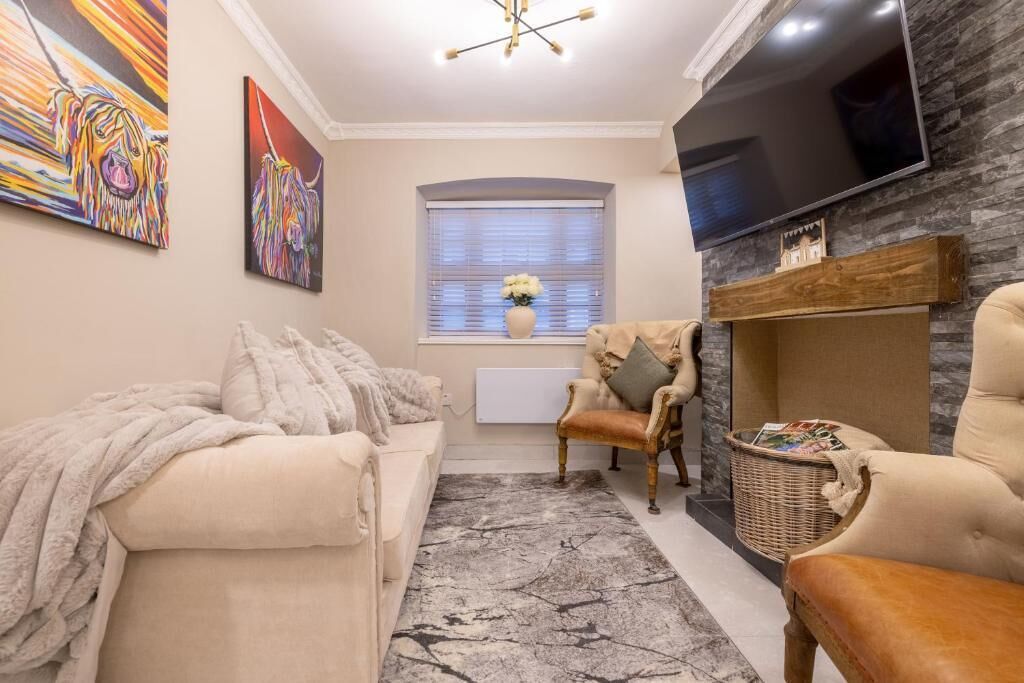 A living room with a sofa, armchairs, a TV, artwork, and a fireplace.