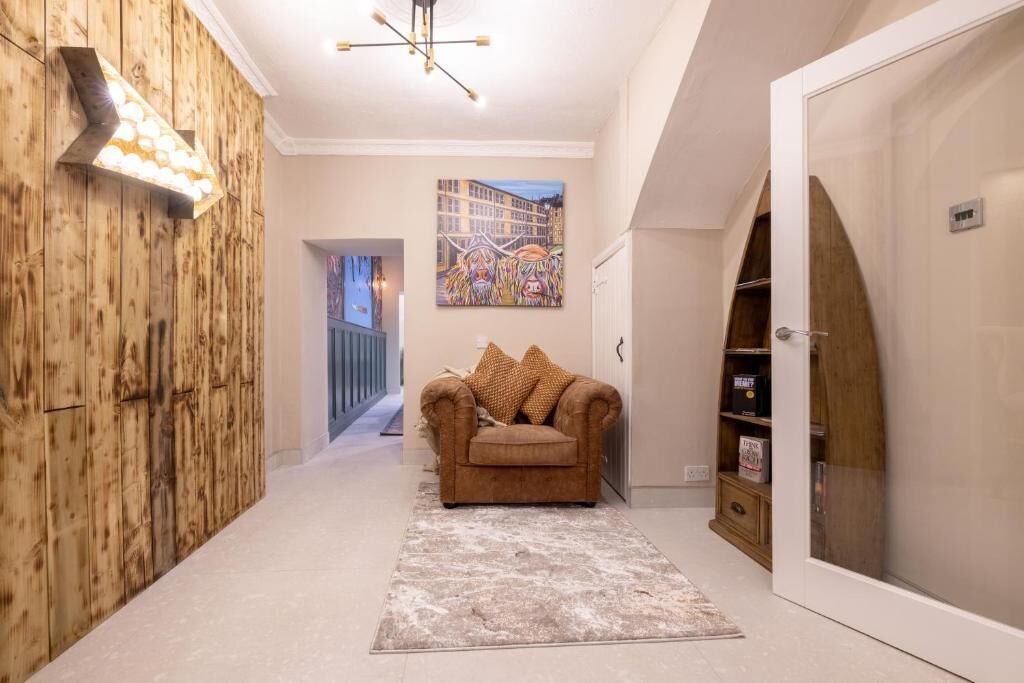 A hallway with a wooden wall, a sofa with cushions, a rug, and a door with a mirror.
