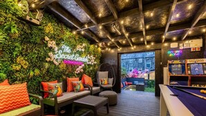 Un jardín interior acogedor con billar, asientos cómodos y un letrero de neón.