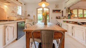 Een rustieke keuken met een houten tafel, stoelen, een hanglamp en uitzicht op het buitengebied.