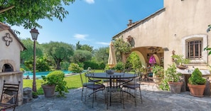 An outdoor patio with a stone table and chairs, surrounded by potted plants and a swimming pool. - Le Mas du Pas de Sénès (La Colle-sur-Loup)