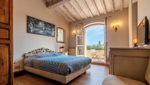 Een slaapkamer met een bed, een schilderij, een deur naar een buitenruimte en uitzicht op de lucht.