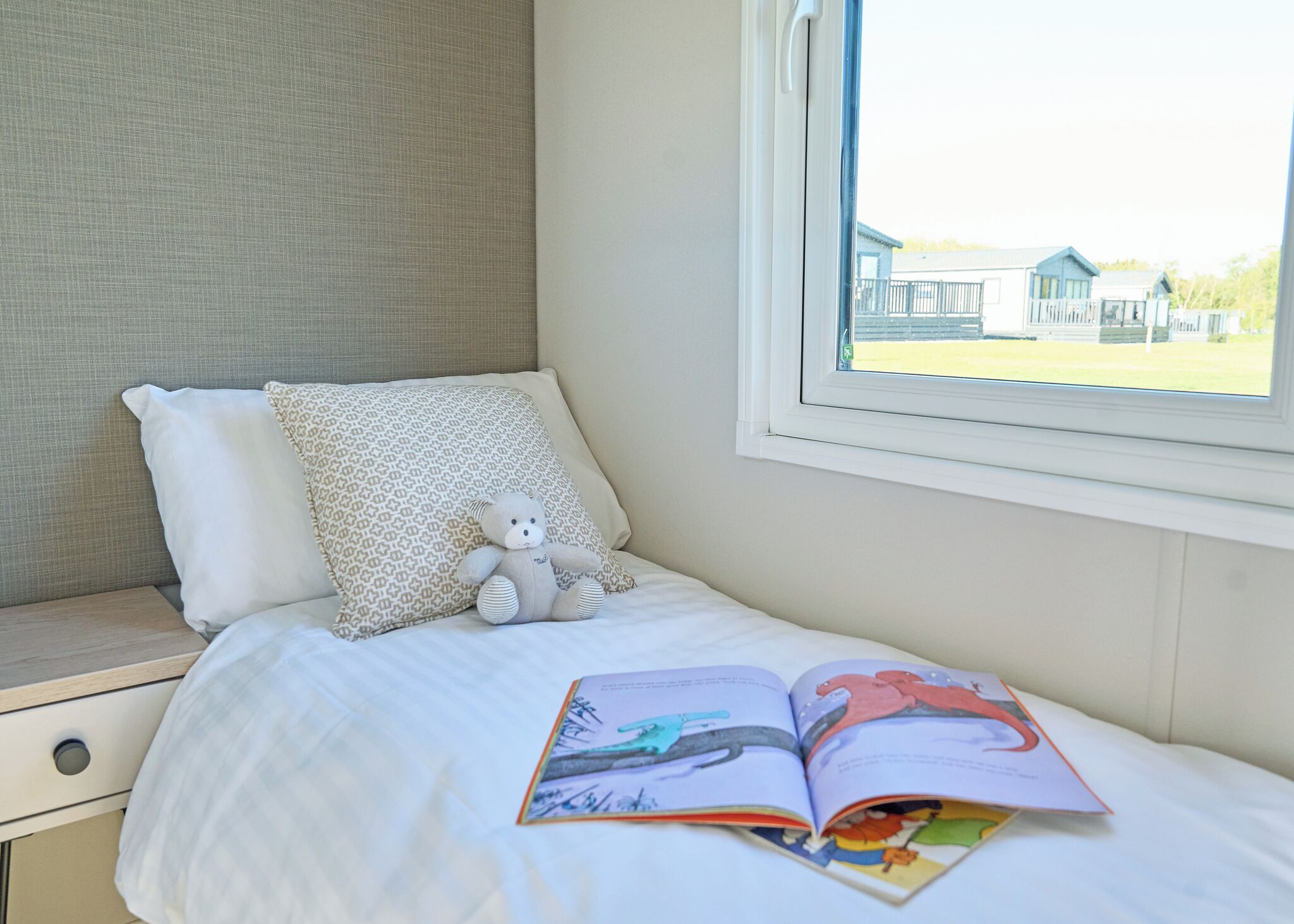 A bedroom with a bed, a window, a teddy bear, and an open book.