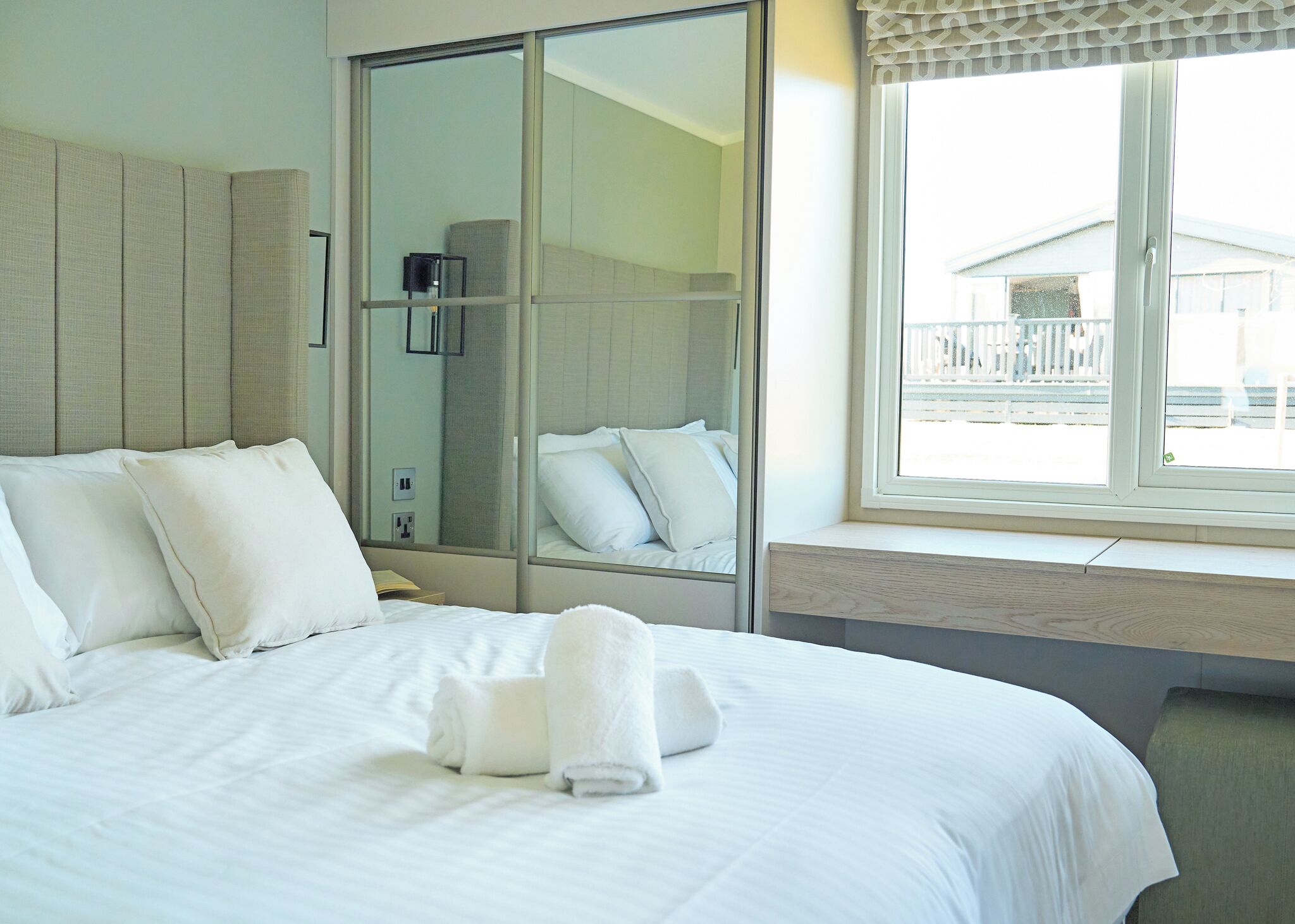 A hotel room with a bed, a large mirror, a bedside table, and a window with a view of the outside.