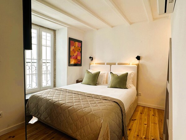 A bedroom with a bed, a window, a painting, and wooden flooring.