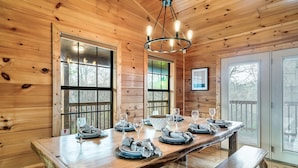 Ein Holzinterieur mit einem für sechs Personen gedeckten Esstisch, großen Fenstern und einer Chandelier.
