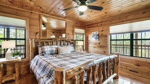 Ein Schlafzimmer einer Holzhütte mit Bett, Deckenventilator, Fenster und Spiegel.