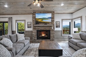 A living room with a stone fireplace, a television mounted above it, and two sofas with patterned cushions. - 4BR Luxury Cabin / Panoramic Mt Views / Game Rm, Bunk Rm, Playground, Firepit (Gatlinburg)
