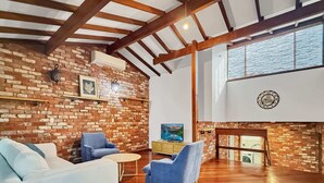 A spacious living room with a brick wall, wooden beams, a fireplace, and a television. - Peaceful 3-Bed Stay Near the Coast (Bouvard)