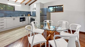 A modern kitchen with white cabinetry, a glass dining table, and white chairs. - Peaceful 3-Bed Stay Near the Coast (Bouvard)
