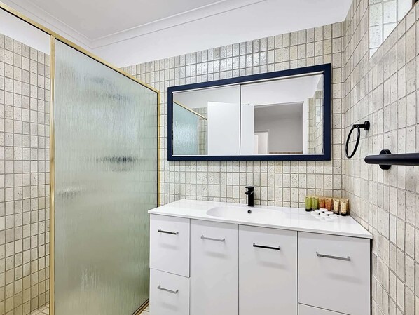 A bathroom with a white sink, a mirror, and a shower area.