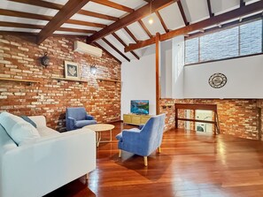 A living room with a brick wall, wooden beams, a sofa, two armchairs, a coffee table, a TV, and a fireplace.