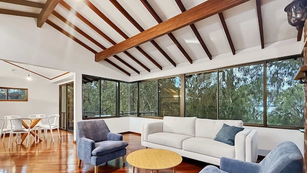 A modern living room with a white sofa, blue armchairs, a round wooden coffee table, and large windows offering a view of trees. - Peaceful 3-Bed Stay Near the Coast (Bouvard)