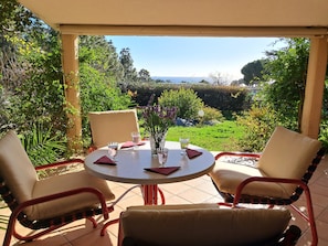 Eine Terrasse mit Tisch und Stühlen, eine Vase mit Blumen und Blick auf Grünflächen sowie eine ferne Landschaft.
