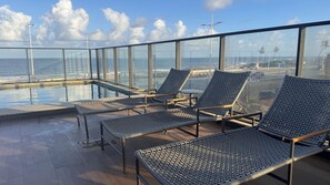 Ein Poolbereich auf dem Dach mit Liegestühlen und Blick auf den Ozean.