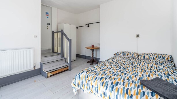 A bedroom with a bed, a small table, and a staircase leading to another room. - Room 1 - The Archers (Southampton)