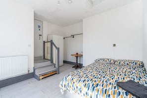 Un dormitorio con una cama, una mesita y una escalera que lleva a otra habitación.