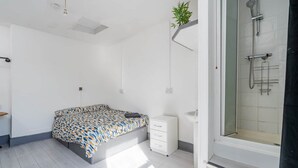 A bedroom with a bed, a bedside table, a small cabinet, a shower area, and a potted plant. - Room 1 - The Archers (Southampton)