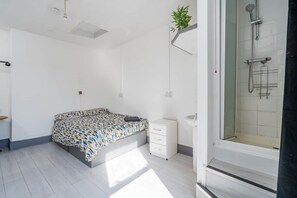 Un dormitorio con cama, mesita de noche, un armario pequeño, zona de ducha y una planta en maceta.