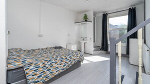 A modern bedroom with a bed, a small white dresser, a bathroom with a sink and shower, and a staircase leading to an outdoor area. - Room 1 - The Archers (Southampton)