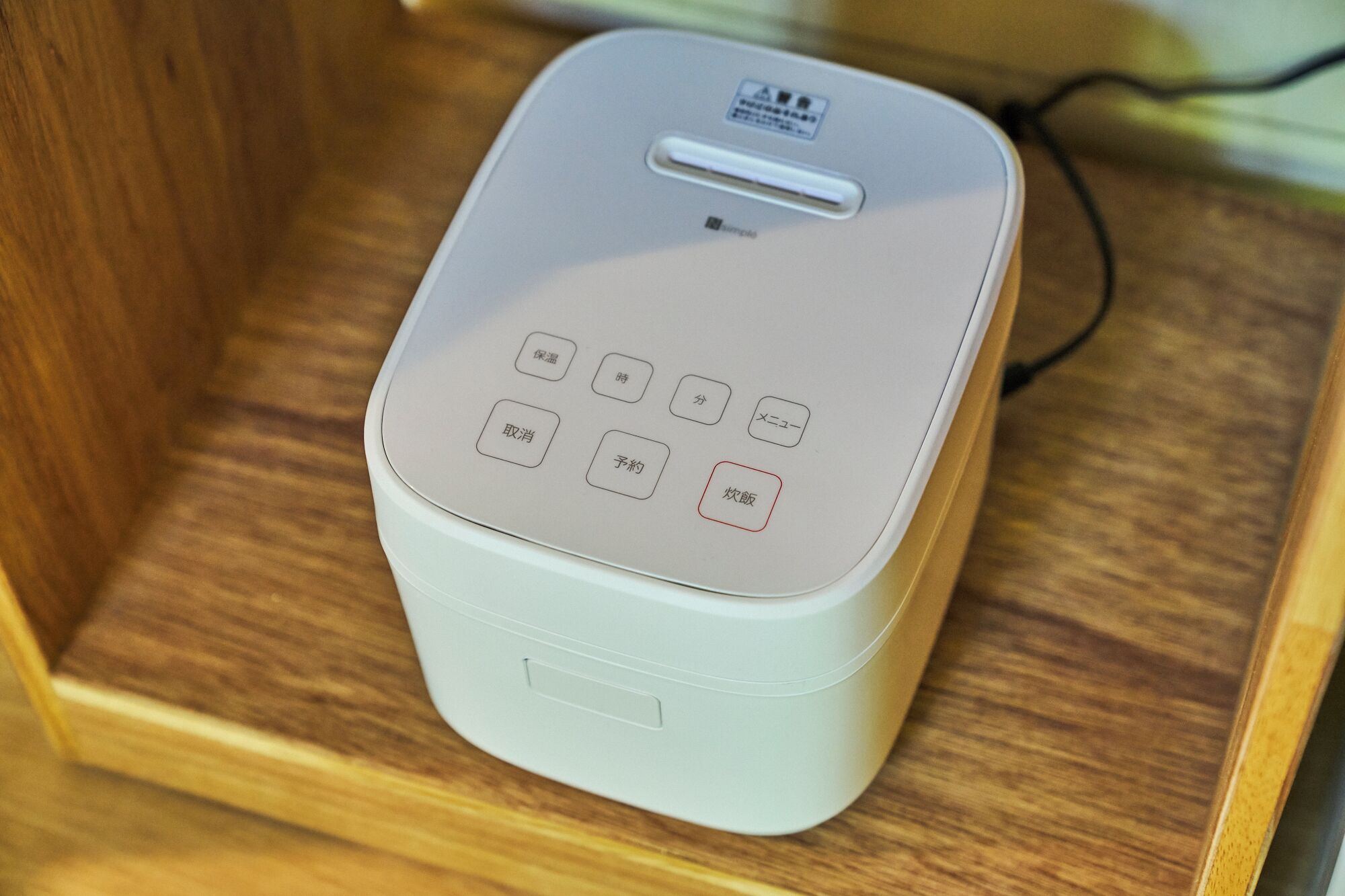 A white electronic device with a label and several buttons on its front panel, placed on a wooden surface.