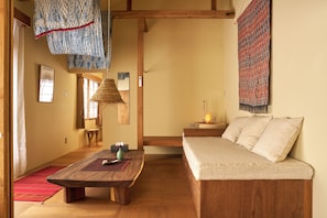 A room with a wooden sofa, a wooden dining table, a hanging woven basket, and a wall-mounted lamp. - Kaneko sanso KK1 (Hokuto city Oizumi cho Nishiide)