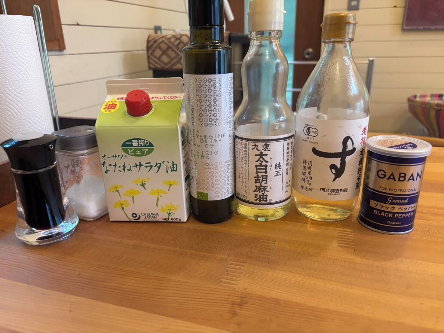 Une table sur laquelle se trouvent divers articles, notamment un carton de lait, des bouteilles d’huile, un récipient de poivre noir et un thermos.