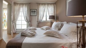 Un lit bien fait, avec du linge de lit blanc, une lampe de chevet et un tableau encadré au mur.