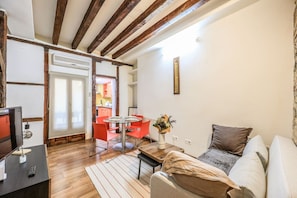 Een woonkamer met een bank, een salontafel, een televisie en een eethoek met een tafel en stoelen.