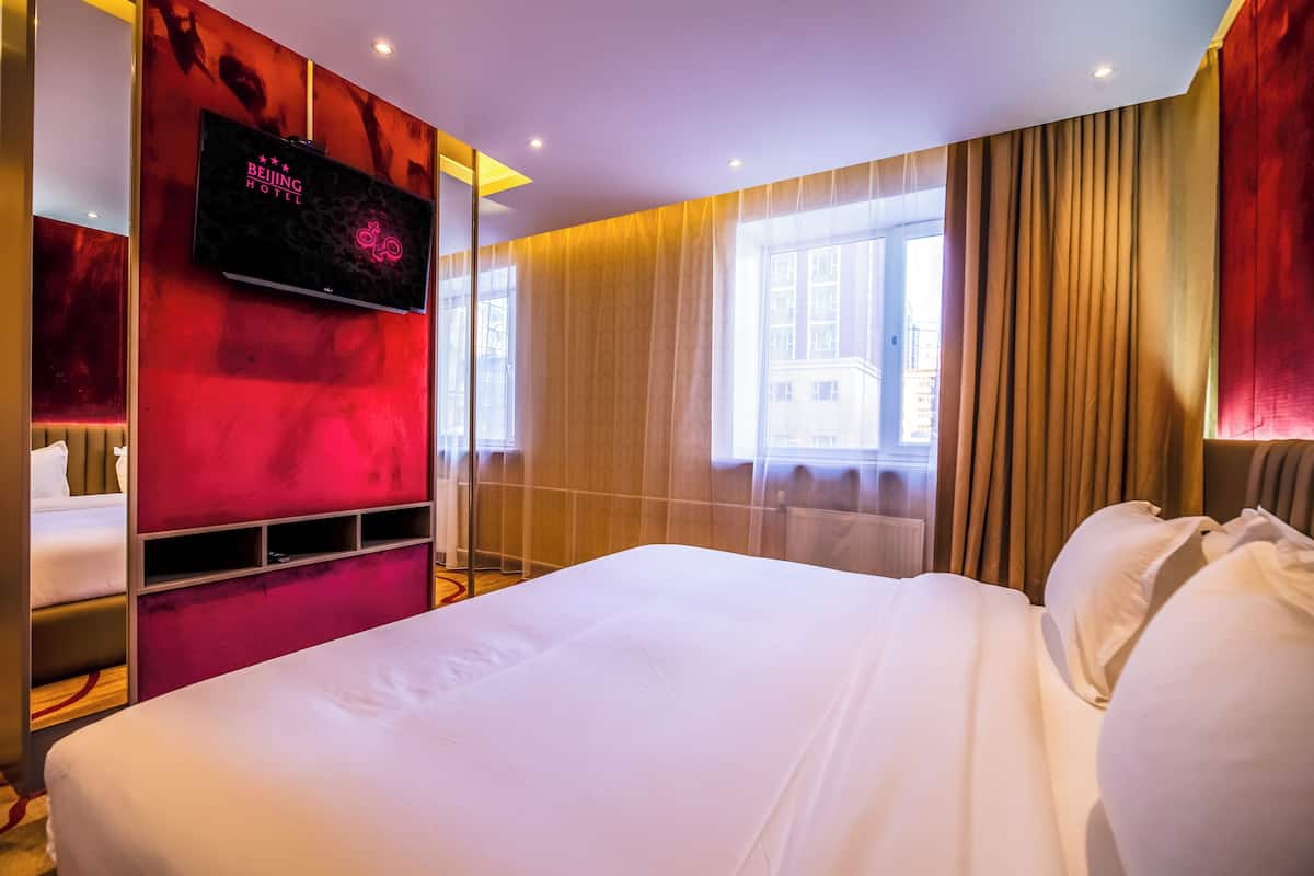 Hotellihuone, jossa on sänky, seinälle asennettu televisio ja ikkuna, jossa on verhot.