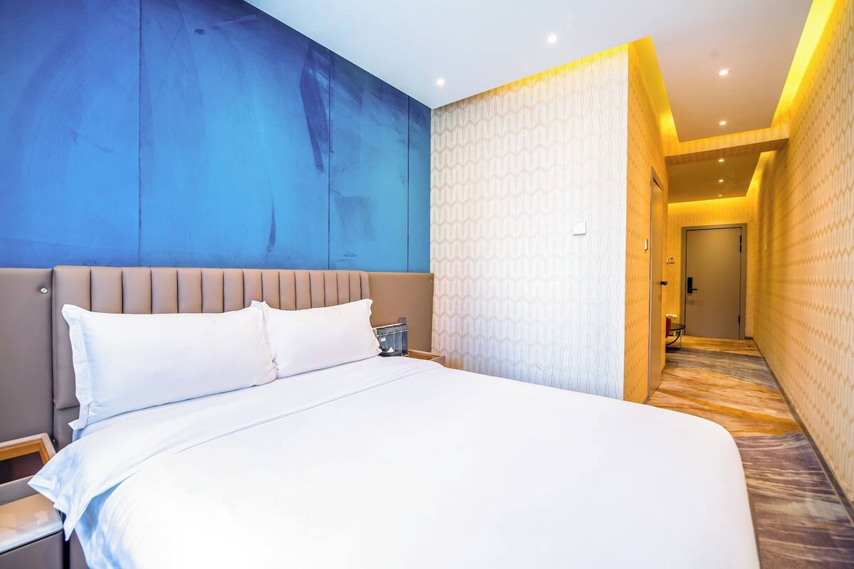 Hotellihuone, jossa on suuri sänky, sängynpääty, yöpöytä ja yökaappi.