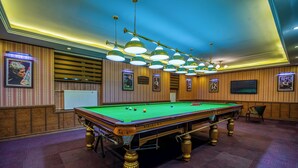 Ein Billardtisch mit grüner Spielbahn, umgeben von Holzvertäfelung und gerahmten Bildern an den Wänden.