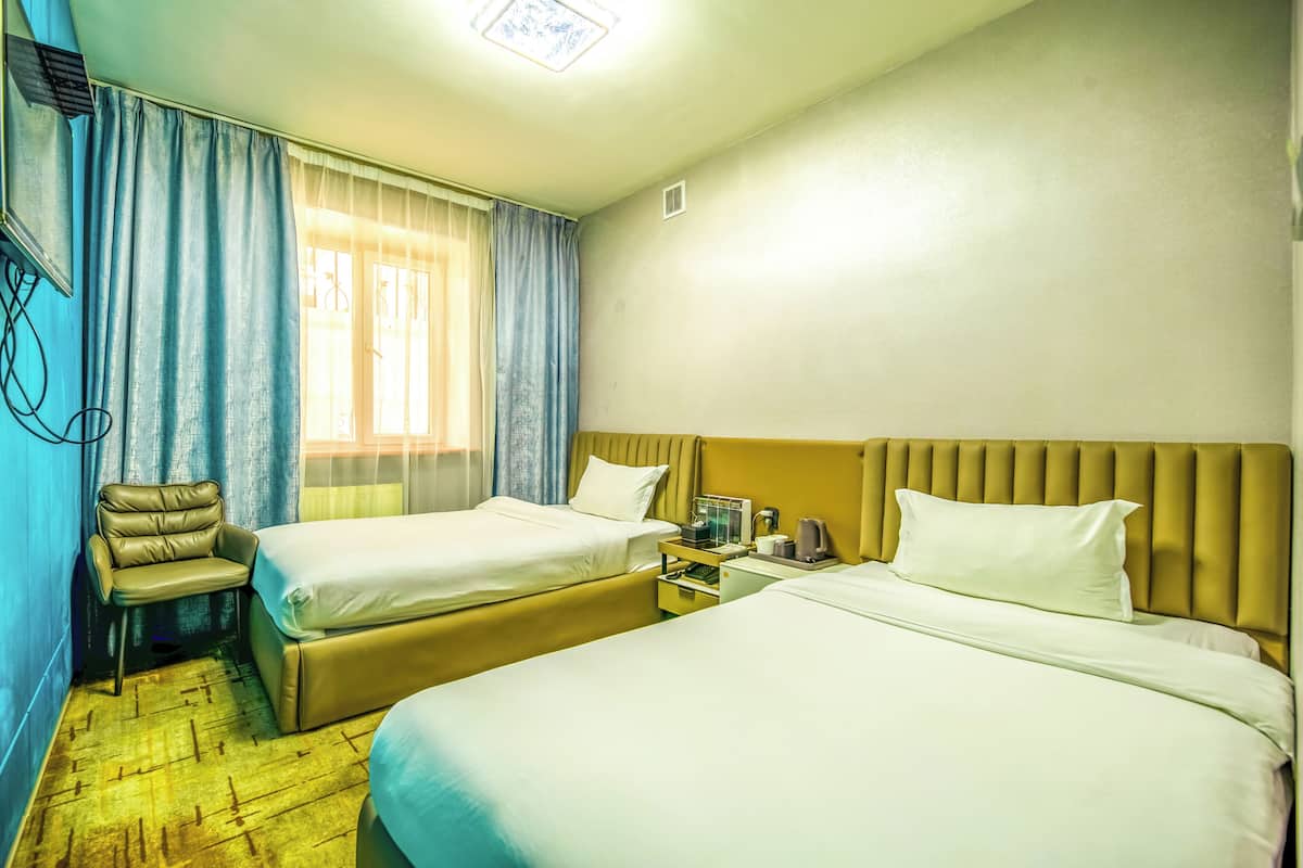 Hotellihuone, jossa on kaksi sänkyä, tuoli, yöpöytä ja ikkuna, jossa on verhot.