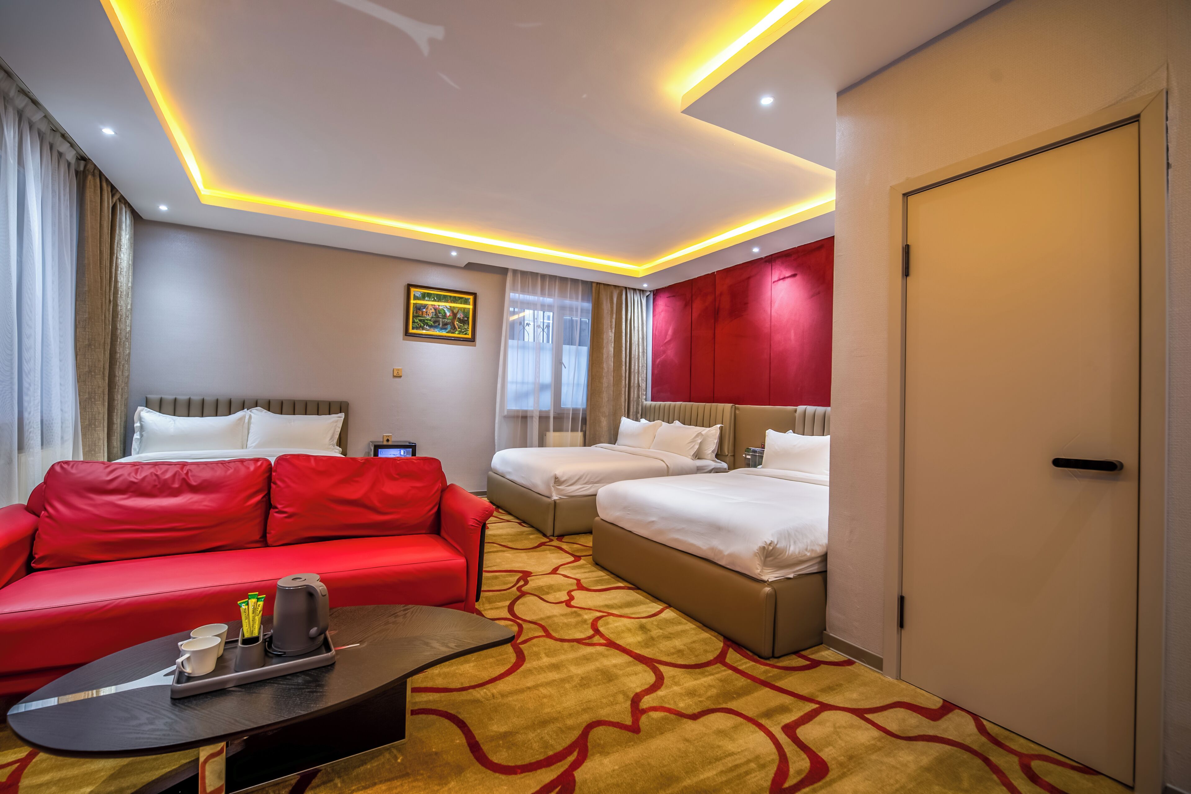 A hotel room with a red sofa, two single beds, a coffee table, and a door.