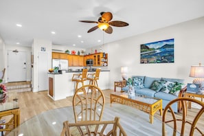 A modern kitchen with wooden cabinets, a dining area with wicker chairs, a blue sofa, and a ceiling fan. - Napili Point | 2 Water Front Villas, Sleeps 8 | Car Incl. w/ 6 nights | ML-4025 by KBM (Lahaina)