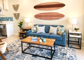 Een woonkamer met een blauwe bank, twee bijzettafels, een salontafel en een vloerkleed met een patroon.