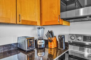 A kitchen with wooden cabinets, a toaster, a blender, a knife block, and a stove. - Napili Point | 2 Water Front Villas, Sleeps 8 | Car Incl. w/ 6 nights | ML-4025 by KBM (Lahaina)