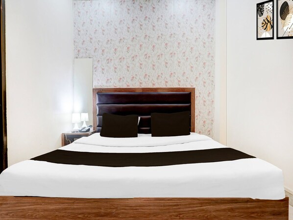 Een net opgemaakt bed met een donkere hoofdbord, een witte dekbedovertrek en twee donkere kussens.