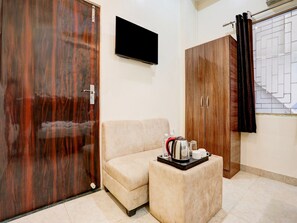 Ein Zimmer mit einer Couch, einem kleinen Tisch mit Wasserkocher und Tassen, einem Fernseher und Holzschränken.
