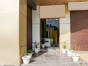 A modern building entrance with potted plants, a tiled pathway, and closed shutters. - Deluxe Sankat Mochan Gandhi Nagar (Varanasi)